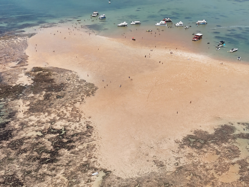 Grupo de pessoas caminhando sobre o banco de areia seca no meio do oceano.