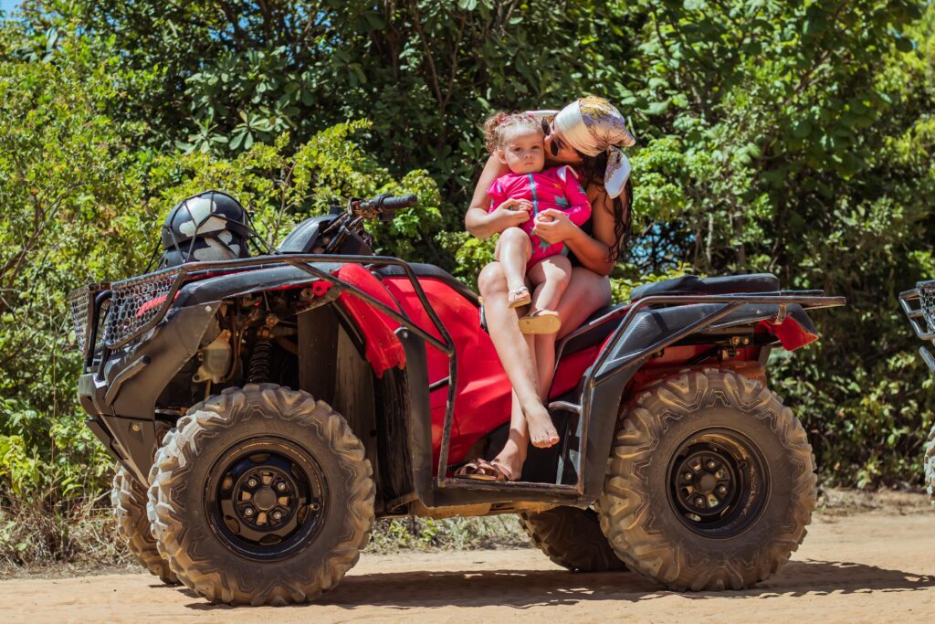 Turista em pé em cima do quadriciclo com os braços abertos celebrando a vista do mar ao fundo.