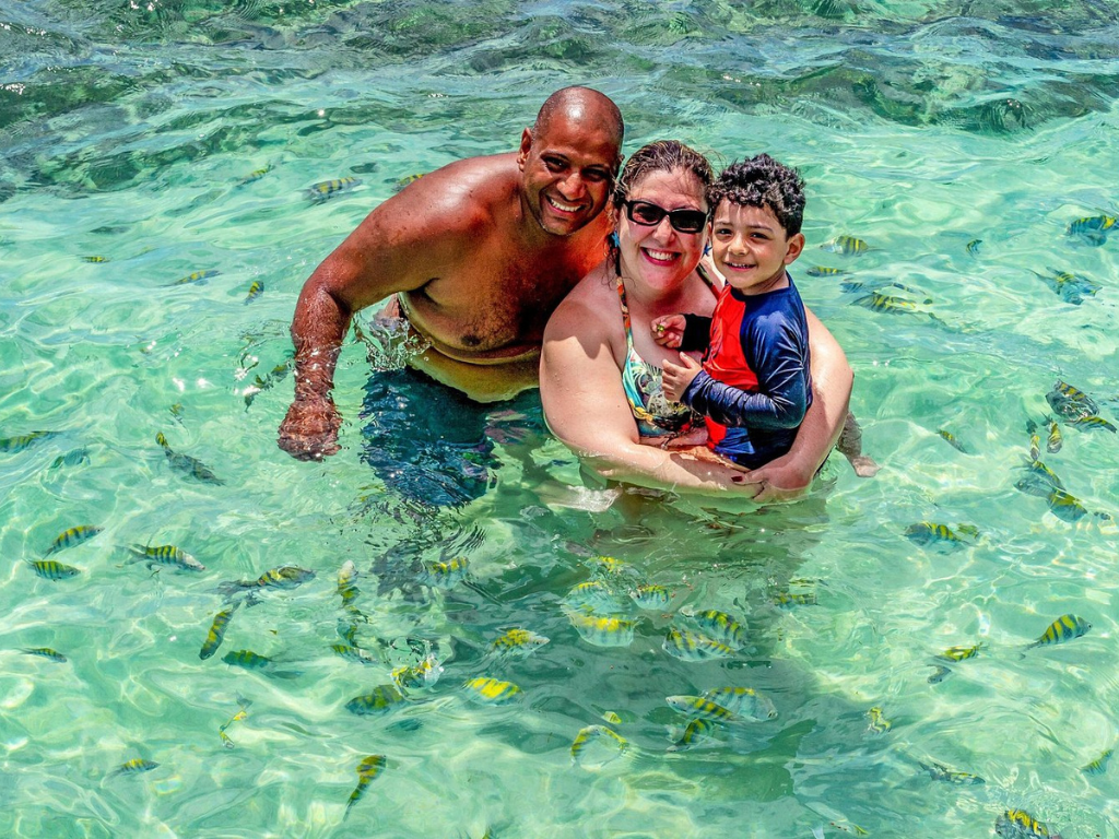 Mulher tirando selfie no barco com chapéu de praia e óculos escuros, sorrindo.