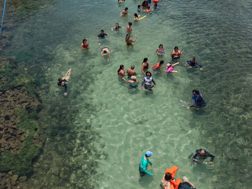 Família com crianças sorrindo e usando coletes salva-vidas nas águas rasas das Piscinas de Picãozinho.
