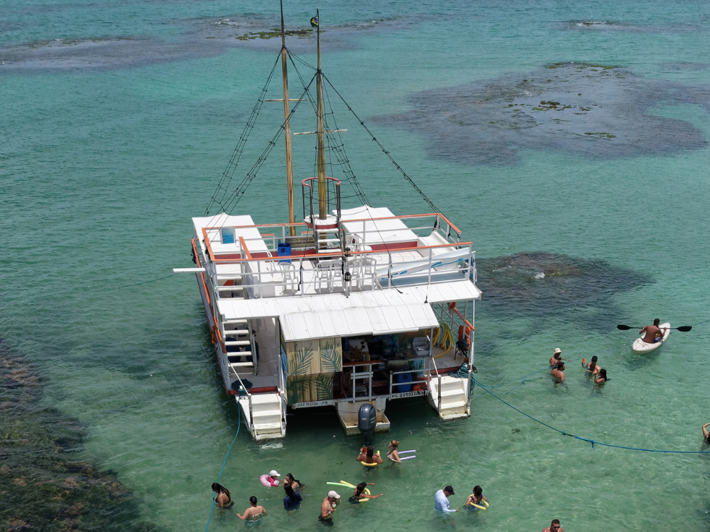Estrutura do catamarã da Paraíba Náuticos ancorado nas Piscinas do Seixas, equipado com toboágua e turistas se divertindo.