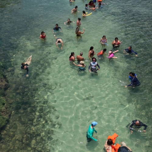 Família com crianças sorrindo e usando coletes salva-vidas nas águas rasas das Piscinas de Picãozinho.