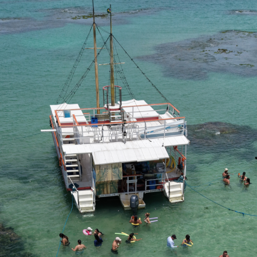Estrutura do catamarã da Paraíba Náuticos ancorado nas Piscinas do Seixas, equipado com toboágua e turistas se divertindo.