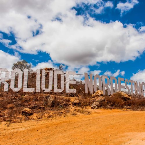 Casal sorrindo e tirando foto no letreiro famoso escrito Roliúde Nordestina na entrada da cidade de Cabaceiras.