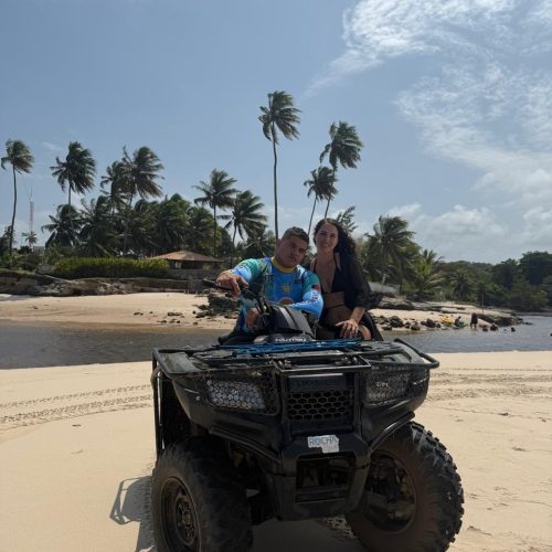 Turista pilotando quadriciclo em uma trilha de terra vermelha levantando poeira.