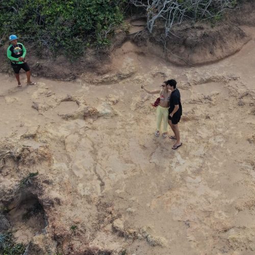Casal usando capacetes de segurança sorrindo em cima do quadriciclo durante passeio no Litoral Sul.