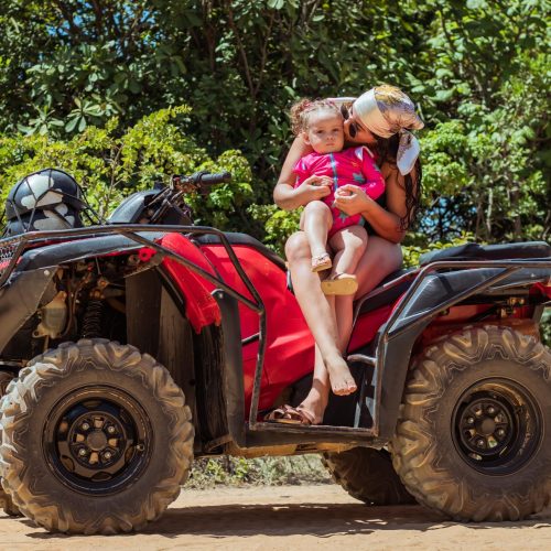 Turista em pé em cima do quadriciclo com os braços abertos celebrando a vista do mar ao fundo.